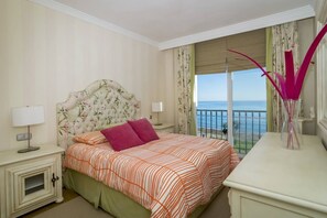 A hotel room with a bed, a nightstand, a dresser, a window with a view of the sea, and a balcony. - HB - Comfortable Beachfront Holiday Apartment (El Velerín)