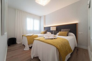 Quarto de hotel com duas camas, mesa de cabeceira, luminária e janela com cortinas.