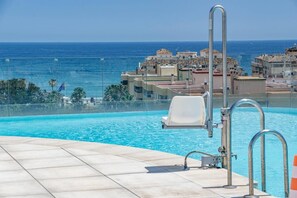 En swimmingpool med utsikt över havet och byggnader i bakgrunden.