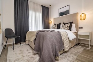 A modern bedroom with a bed, a chair, a bedside table, and a hanging light fixture. - PR - Stunning flat front line beach Puerto Banus (Marbella)