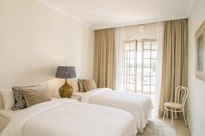 A hotel room with two beds, a nightstand, a lamp, a chair, and a window with curtains. - AP116 - Casa Aloha l by Roomservices (Marbella)
