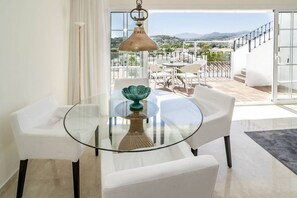 A modern dining area with a glass table and white chairs, a decorative bowl, and a view of a balcony with outdoor seating. - AP116 - Casa Aloha l by Roomservices (Marbella)