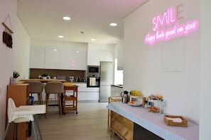A modern kitchen with white cabinets, a neon sign, and a dining area with chairs and a table. - PI Silveira Farm •Nature & Tranquility (double room) (Loulé)