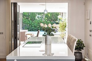 A modern dining area with a white table, a vase with flowers, and a view of greenery outside. - Villa Nottingham Stunning private villa (Marbella)
