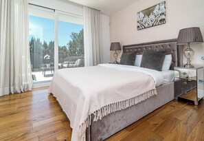 A bedroom with a large bed, two bedside lamps, a nightstand, and a view of a balcony. - Villa Nottingham Stunning private villa (Marbella)