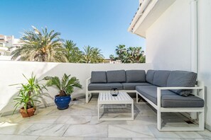 En tagterrasse med en grå hjørnesofa, et hvidt sofabord og plantekasser.