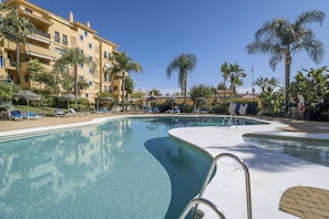 Ein Swimmingpool mit Liegestühlen und Palmen, umgeben von einem Hotelgebäude.