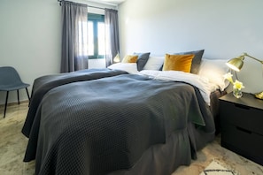 Une chambre avec deux lits, une chaise, une table de chevet avec une lampe et une fenêtre avec des rideaux.