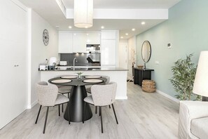 Una cocina moderna con armarios blancos, una isla central y un comedor con una mesa redonda y sillas.