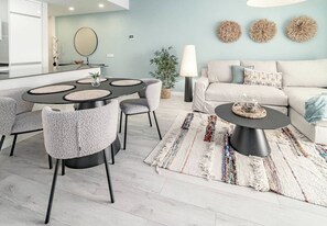 A modern living room with a round dining table, grey upholstered chairs, a sofa, a coffee table, and a patterned rug. - LE2E- Modern new-build flat near the beach (Estepona)