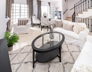 Ein modernes Wohnzimmer mit einem Glastisch, weißen Sofas und einer Treppe.
