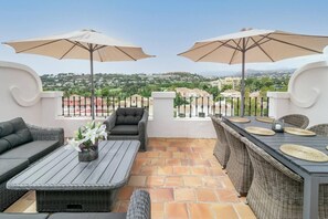 Eine Terrasse mit Gartenmöbeln, zwei Sonnenschirmen und Blick auf eine Stadt.