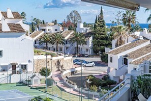 Ein Wohngebiet mit weißen Gebäuden, einem Tennisplatz und Blick auf das Meer.