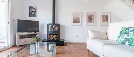 A living room with a TV, a glass coffee table, a sofa, a fireplace, and artwork on the wall.