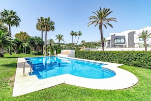 Ein Pool mit geschwungener Kante, umgeben von gepflegtem Rasen und Palmen.