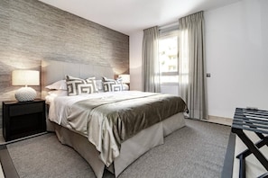 A modern hotel room with a large bed, a bedside table with a lamp, and a view of the outdoors through a window with curtains. - AE - Wonderful apartment in San Pedro centro (San Pedro de Alcantara)