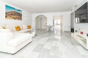 Una sala de estar moderna con un sofá blanco, una mesa de centro de vidrio y un comedor con una mesa y sillas de vidrio.