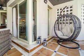A patio area with a wicker chair, a glass door leading to an interior space, and a hanging chair. - FA - Well-equipped apartment in a great location (Marbella)