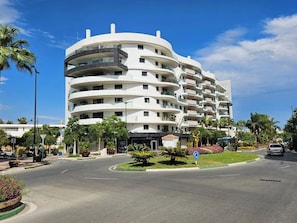A multi-story hotel with a curved facade, a landscaped front yard, and a clear blue sky. - INf11D - Modern city flat near beach & old town (Estepona)