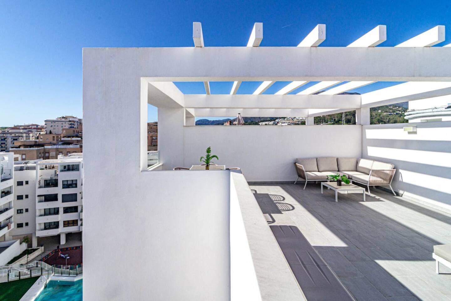 Una terraza en la azotea con piscina, mobiliario exterior y vistas a la ciudad.