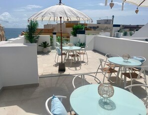 An outdoor patio area with round tables and chairs, a large umbrella, and potted plants. - LE2C Luxury New build apartment near the beach (Estepona)