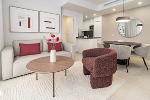 Un saló modern amb un sofà, una taula de centre i un butàc armat amb un dibuix. Hi ha una zona de menjador amb una taula i cadires, i una cuina al fons.