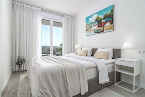 Un dormitorio moderno con una cama grande, una mesita de noche, una ventana con cortinas y un cuadro en la pared.
