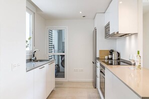 A modern kitchen with a built-in oven, a coffee maker, and a wine bottle on the counter. - JG- Top modern apartment in Nueva Andalucia (Marbella)