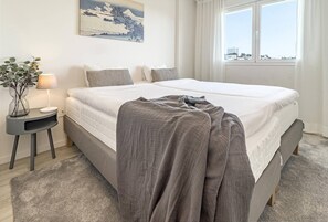 Een hotelkamer met een bed, een nachtkastje met lamp, een raam met uitzicht en een schilderij aan de muur.