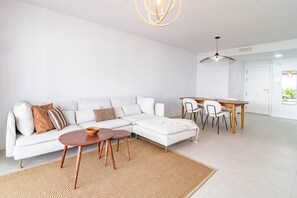 Un saló modern amb un sofà seccional blanc, una taula de centre rodona de fusta i una zona de menjador amb taula i cadires de fusta.