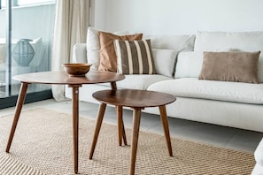 A modern living room with a white sofa, two wooden tables, and a woven rug. - LMe9BA- Modern flat close to beach and port (Estepona)