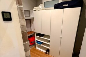 A small storage area with white cabinets, a red storage bin, and a digital thermometer on the wall. - Town Centre Apartment, Mont-Dore (Mont Dore Puy-De--Dome)