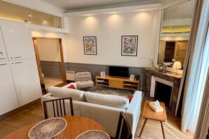 A modern living room with a sofa, TV, and a dining area with a table and chairs. - Town Centre Apartment, Mont-Dore (Mont Dore Puy-De--Dome)