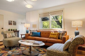 A living room with a sofa, armchairs, a coffee table, and two lamps. - Lively Oak 175 Steps to The Village  Near NCSU (Raleigh)