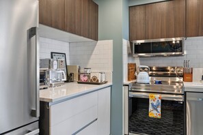 A modern kitchen with stainless steel appliances, white cabinetry, and a tiled backsplash. - Lively Oak 175 Steps to The Village  Near NCSU (Raleigh)
