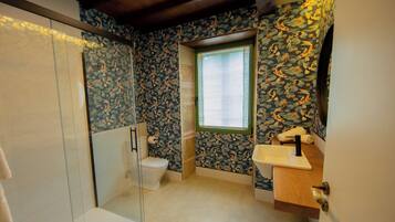 A bathroom with a shower, toilet, and sink, featuring floral wallpaper and a window.