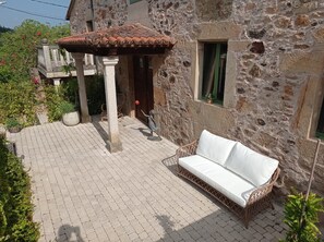 A stone building with a tiled roof, a wicker sofa, and a small garden area. - Vrbo Property (Vila de Cruces)