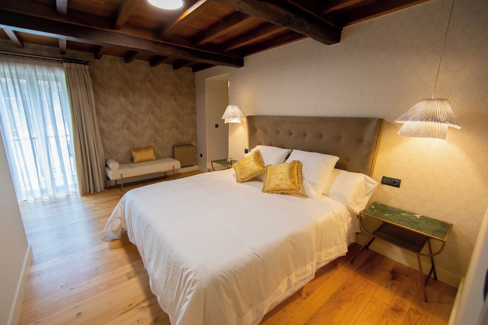 A bedroom with a large bed, two bedside lamps, a nightstand, a sofa, and a window with curtains.