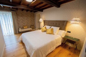 A bedroom with a large bed, two bedside lamps, a nightstand, a sofa, and a window with curtains. - Vrbo Property (Vila de Cruces)