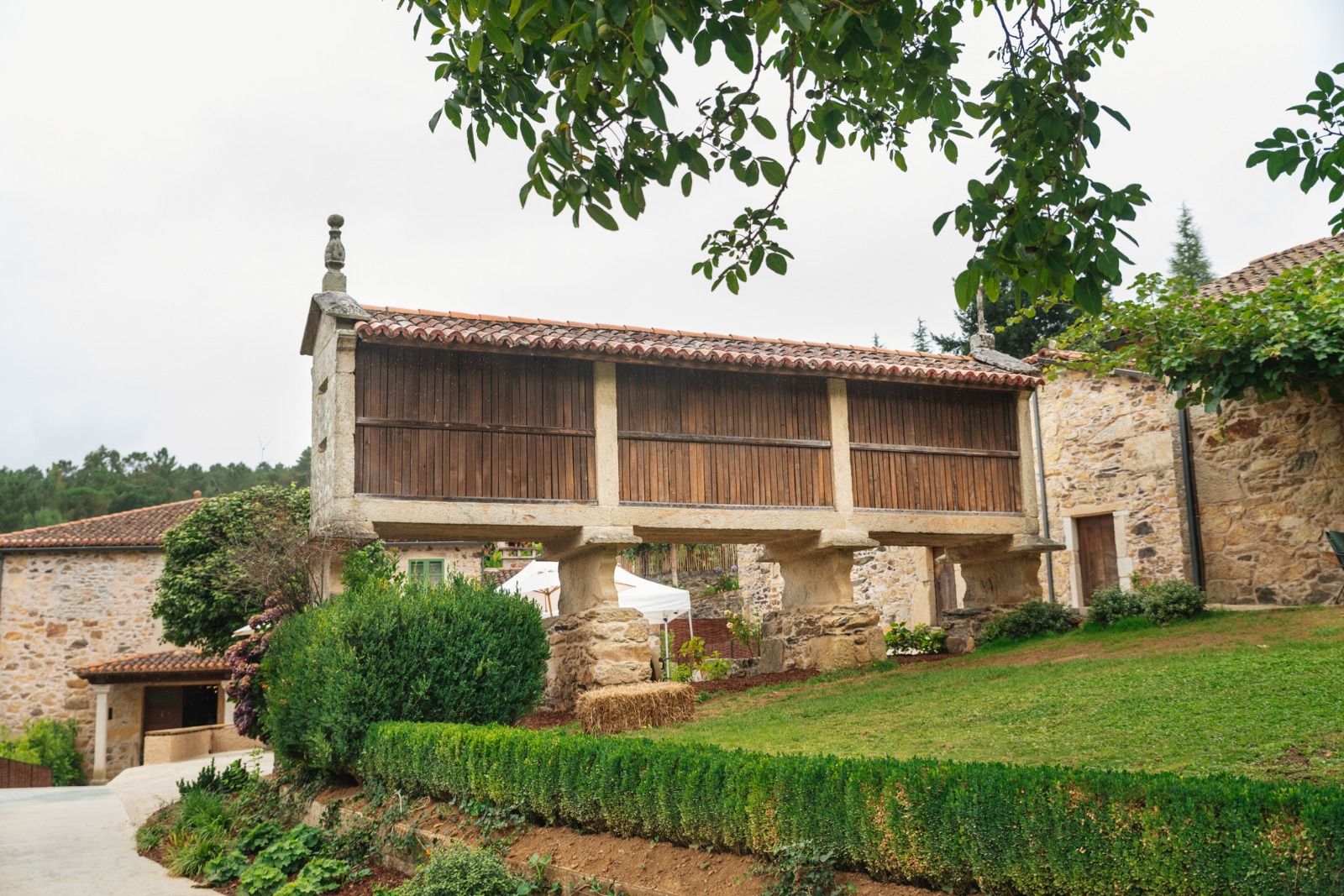 Edifici de pedra amb un balcó de fusta, envoltat de jardins ben cuidats i un cel serè.