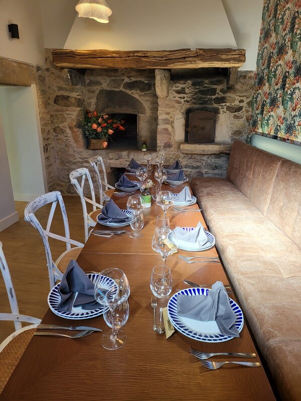 A dining room with a long wooden table set for a meal, stone walls, and a fireplace. - Vrbo Property (Vila de Cruces)