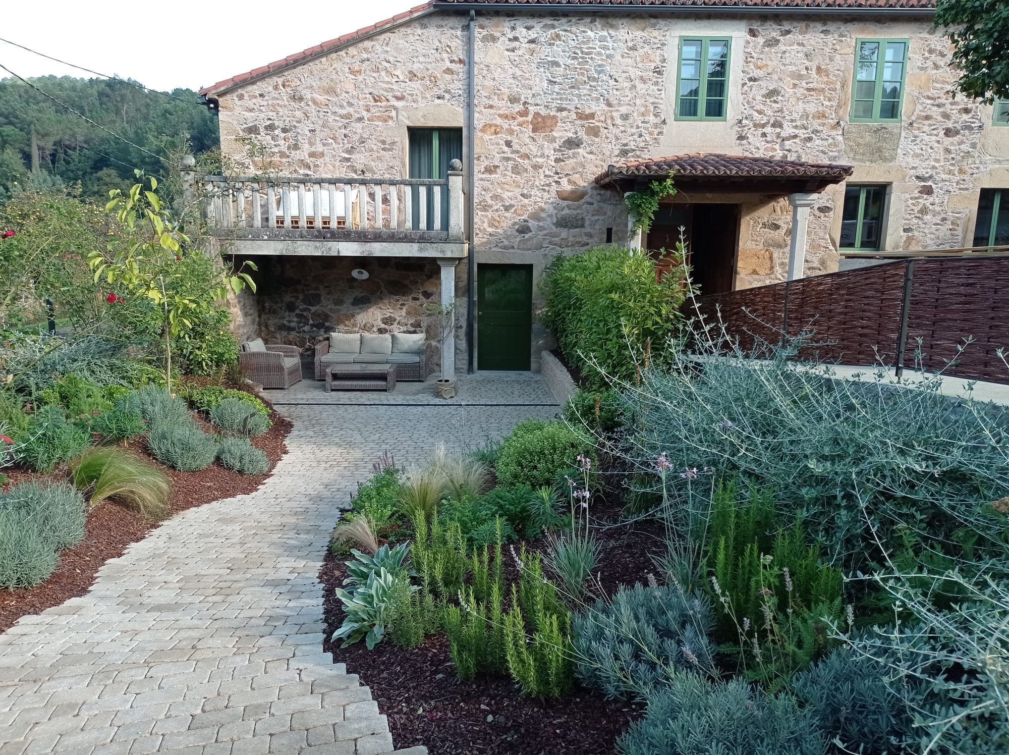 Una casa de piedra con un patio empedrado, mobiliario exterior y diversas plantas.