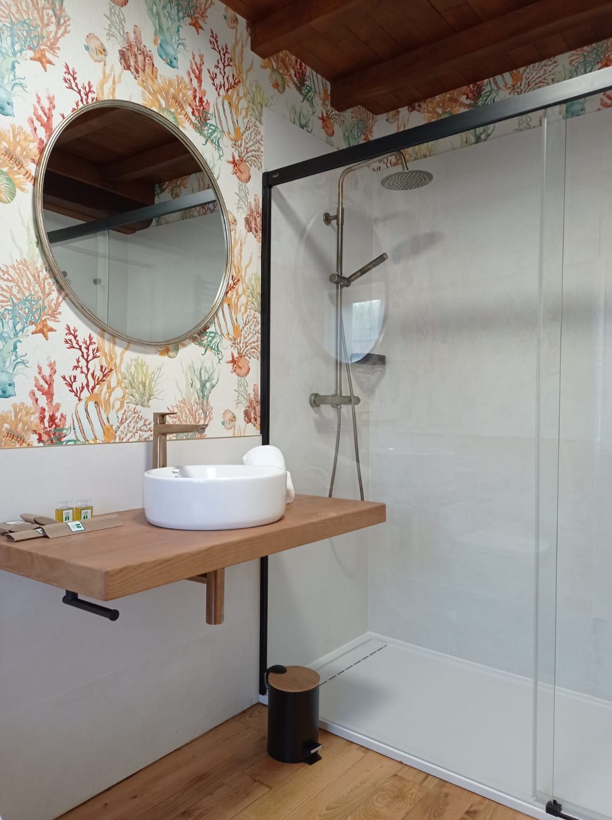 Un baño con un espejo redondo, un tocador de madera, un lavabo blanco y una ducha con mampara de vidrio.