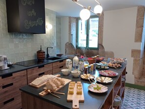 A kitchen with a breakfast buffet featuring bread, pastries, cheese, and fruits.