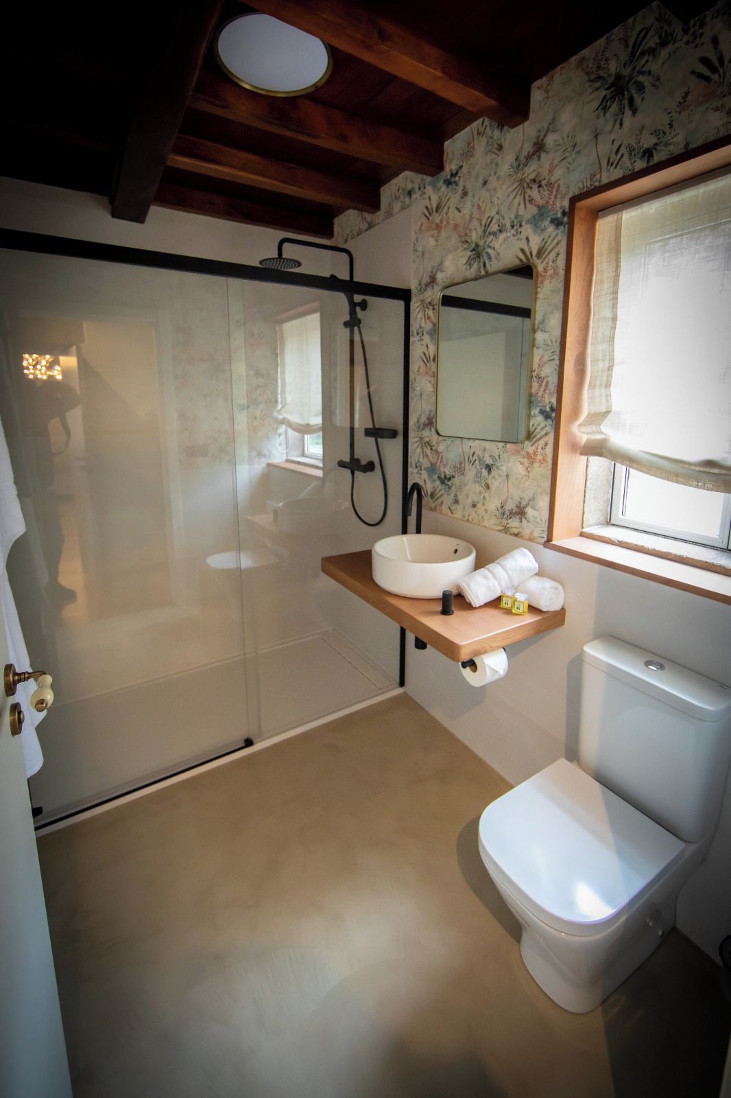 Un bagno con cabina doccia in vetro, un water, un lavandino con specchio e una finestra con tenda.