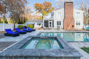 Ein Pool mit Liegestühlen, ein Ziegelkamin und ein Haus mit einer Veranda.