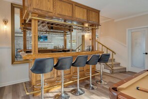 Eine Bar mit Holzhockern, einem Billardtisch und einer Spiegelwand, die den Küchenbereich widerzuspiegeln scheint.