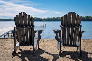 Duas cadeiras Adirondack voltadas para um lago, com um píer ao fundo.
