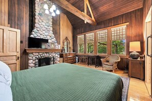 Ein gemütliches Zimmer mit Kamin aus Stein, Holzwänden und großen Fenstern.