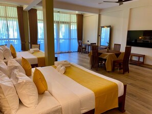 A hotel room with two beds, a dining table, chairs, a TV, and large windows with curtains.
